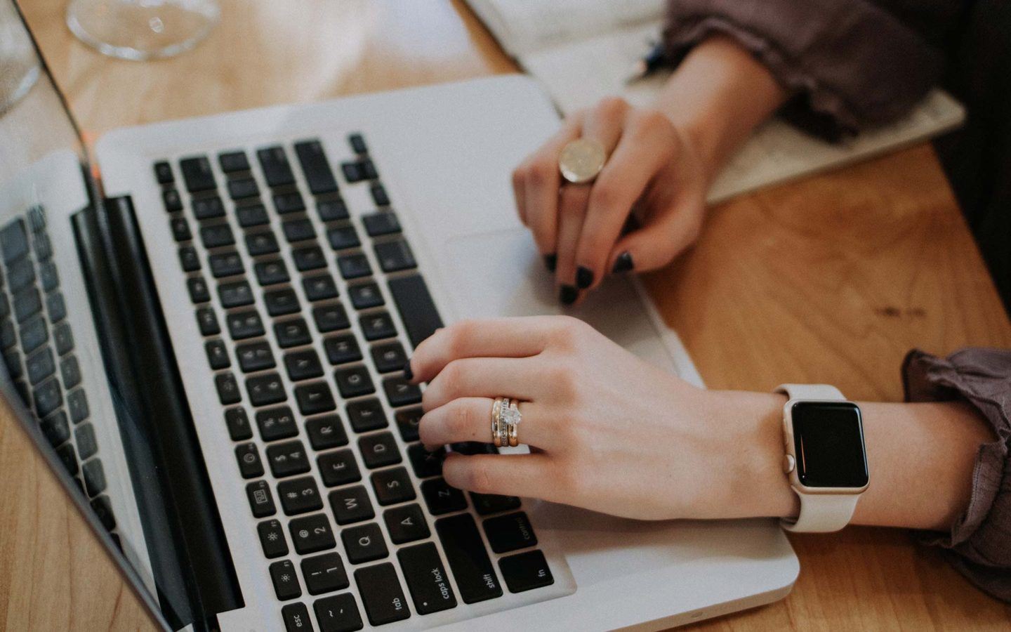 women's hands with watch and rings typing on a silver laptop at a desk